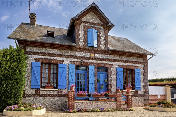 Historic stone house with blue shutters and blooming flowers in decorative plant beds, Historic