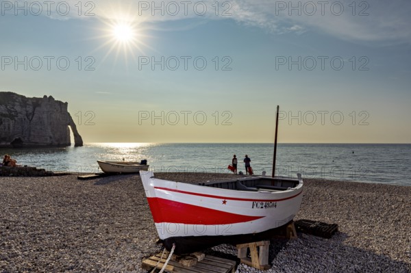 Tranquil beach scene at sunset with boat and people near cliffs, rowing boat at sunset on the coast