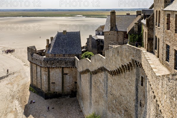 Historic castle wall with a view of a wide expanse of sand and distant buildings under a clear sky,