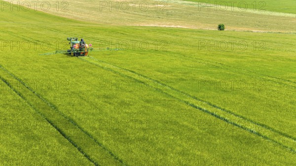 Farmer with tractor working in the field. In early summer, he fertilises the grain for an optimum