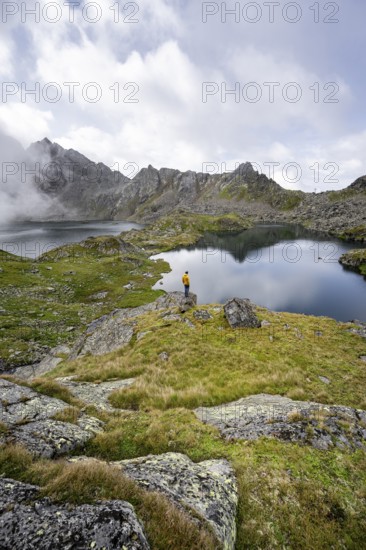 Mountaineer on a rock in front of mountain lakes Wangenitzsee and Kreuzsee, cloudy mountain peaks