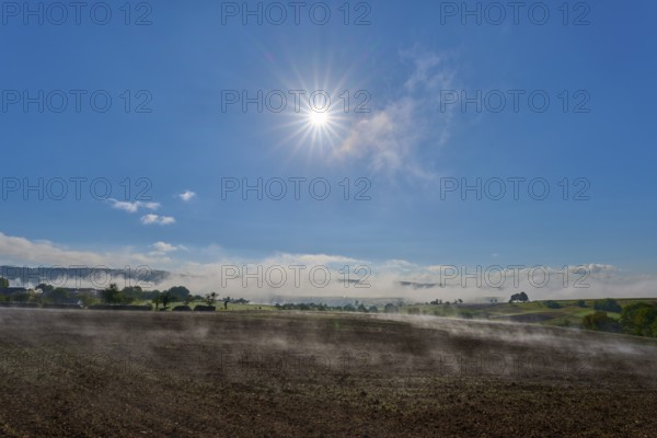 The sun shines brightly over a misty landscape stretching across wide fields, Mönchberg,