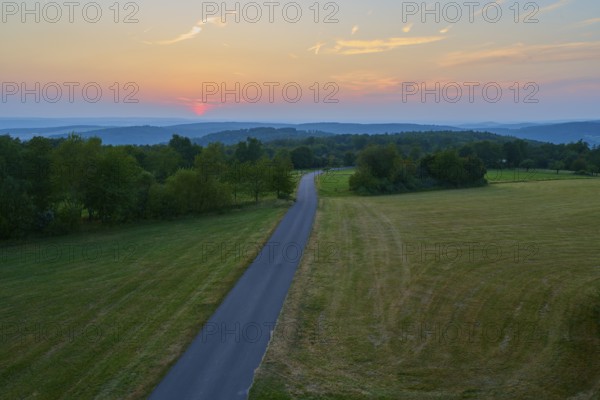 Narrow road winds through fields at sunset with orange sky, Geishöhe, Dammbach, Spessart, Bavaria,