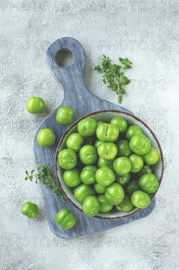 Tkemali, green cherry plum, in a bowl, on a gray table, top view, natural light, no people