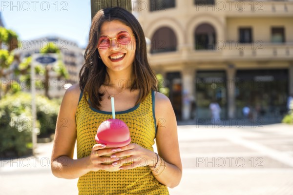 Happy young woman smiling brightly while enjoying a refreshing cold drink on a sunny summer day in