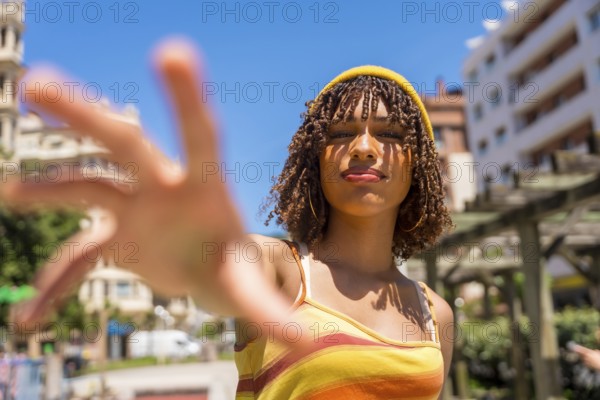 Stylish young woman extending her hand towards the camera in a vibrant city setting, enjoying a
