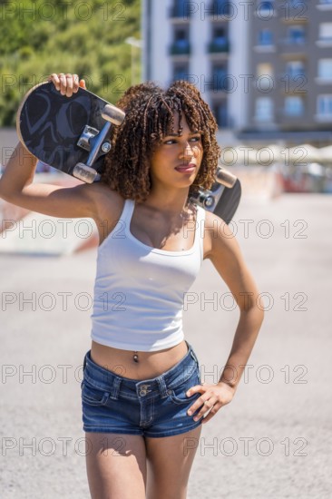 Confident young woman holding skateboard on shoulder, enjoying urban lifestyle and skateboarding