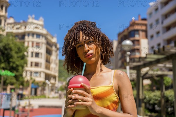 Fashionable young woman enjoys a cold beverage in a vibrant urban setting, embracing the summer