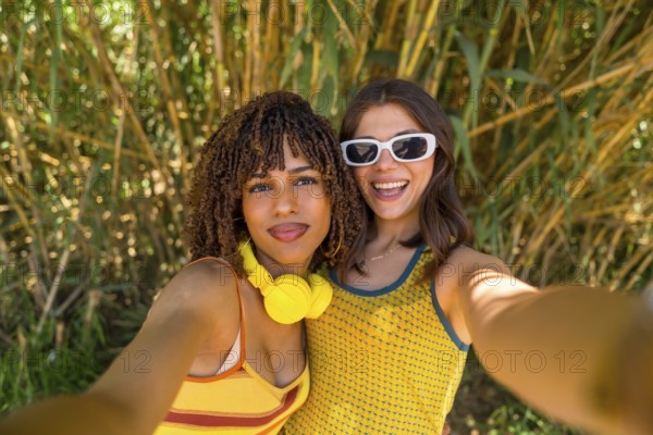 Two smiling girls taking a selfie in front of bamboo plants, wearing yellow clothes and headphones