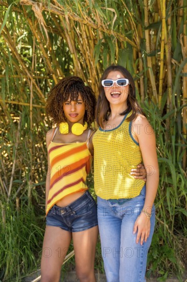 Two female friends hugging and smiling in a vibrant bamboo forest, soaking up the sun and enjoying