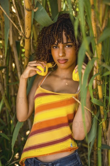Young woman holding vibrant yellow headphones while posing gracefully in a lush bamboo forest,