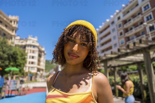 Portrait of a fashionable young woman with curly hair and yellow beanie enjoying a sunny day in an