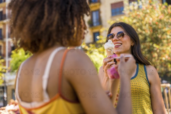 Two friends savoring ice cream cones on a sunny summer day in the city, sharing laughter and
