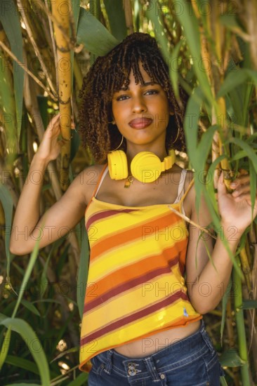 Young woman wearing yellow headphones, posing amidst vibrant bamboo trees, enjoying the soothing