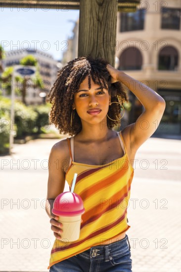 Fashionable young woman enjoying a sunny day in the city, holding a refreshing beverage and