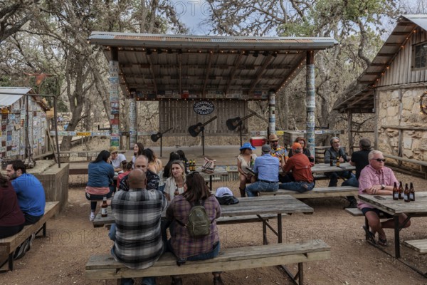 Tourists drinking beer at an open-air bar with a bandstand in Luckenbach, Texas, USA