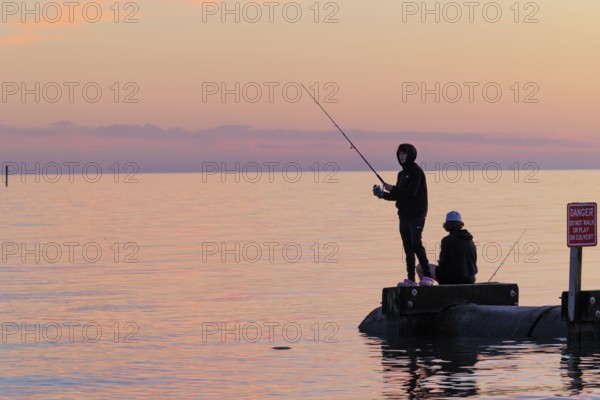 Silhouette of young adults ignoring danger sign while fishing on storm drain culvert in Long Beach,