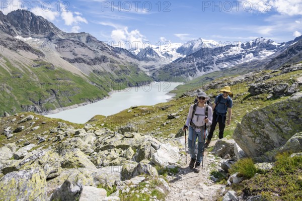 Mountaineer on a hiking trail at a blue mountain lake, reservoir Lac des Dix, behind mountain peak