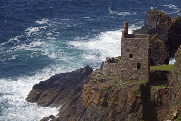 An old stone house perched on cliffs above a stormy sea with crashing waves, engine room, mining,