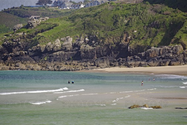 Small waves rolling towards a sandy beach with rocks, people enjoying the water, St Ives, Cornwall,