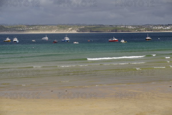 Several boats floating on a calm sea in front of a misty coastline, St Ives, Cornwall, England,