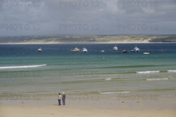 Boats anchored on calm waters off a wide, deserted sandy beach, St Ives, Cornwall, England, United