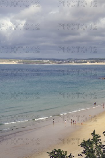 Several people walking on a quiet sandy beach, the sea under a cloudy sky, St Ives, Cornwall,