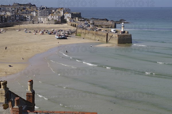 Coastal town with harbour and lighthouse, boats on the beach and gentle waves in the blue sea,