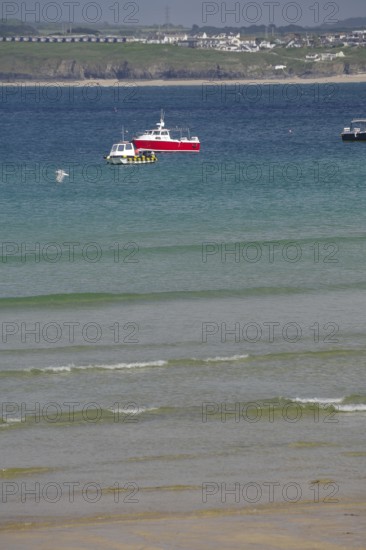 A red boat floats on calm blue water near a wide sandy beach, St Ives, Cornwall, England, United