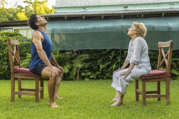 Senior woman and personal trainer engaging in seated exercises on chairs in a serene garden,