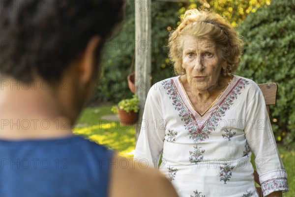 Elderly woman sitting comfortably on a wooden chair in a garden, engaging in a heartfelt