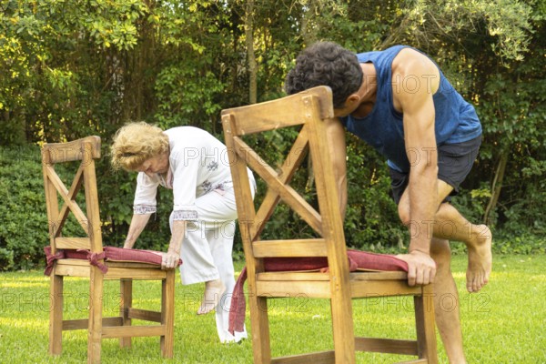 Senior woman and her personal trainer practicing a fitness routine using chairs as support in a