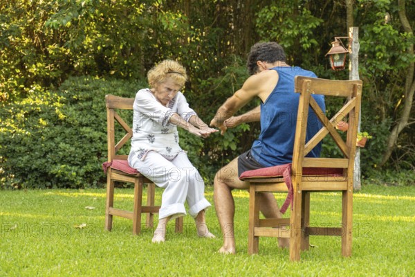Elderly woman practicing physiotherapy with a personal trainer, performing exercises while sitting