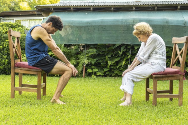 Senior woman and her physiotherapist are performing physical therapy exercises sitting on chairs in