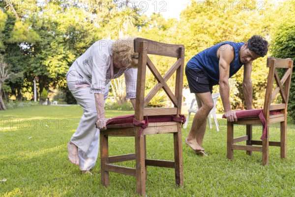 Senior woman and her physiotherapist are performing a rehabilitation exercise using chairs in a