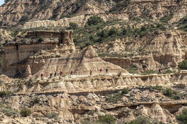 Group of hikers at colorful sandstone rock formations, desert, along gravel road Ruta Jubierre,