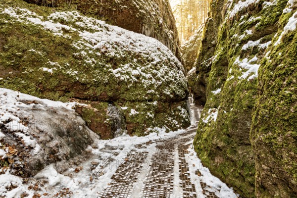 Snow-covered path between moss-covered rock faces in a quiet winter gorge, the Dragon Gorge near