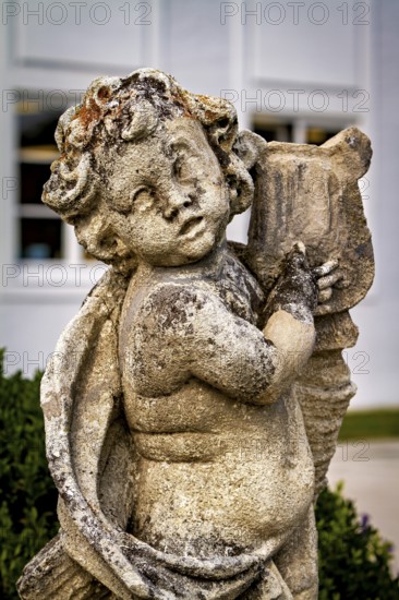 Weathered stone statue of an angel child with wings and background outdoors, stone statues in the