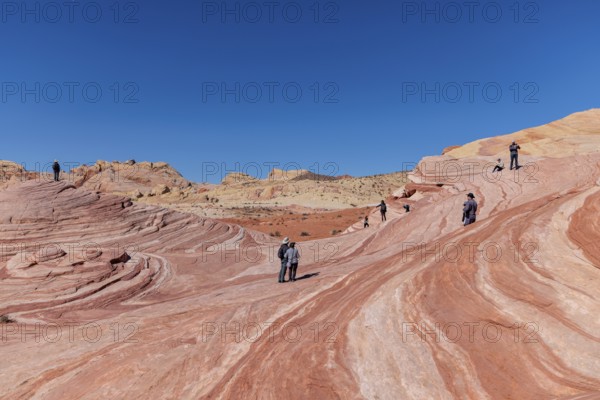 Hikers on a layered sandstone rock formation in the Fire Wave area of Valley of Fire State Park