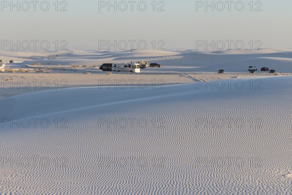 Cars and RVs in a parking area behind a rippled white gypsum sand dune at White Sands National Park