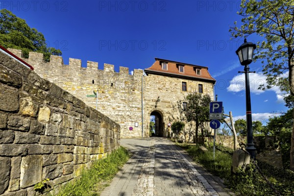 Stone entrance to a castle with cobblestone street and blue sky in the background, The Creuzburg in
