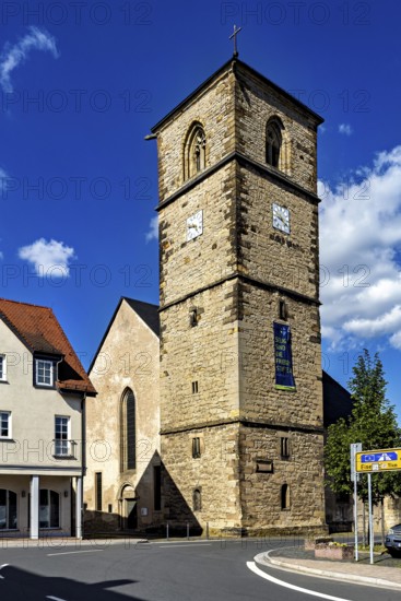Historic stone church tower with clock in front of a blue sky, surrounded by modern buildings, The