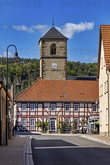 A half-timbered house with a church tower in the village, shining under a blue sky, The church