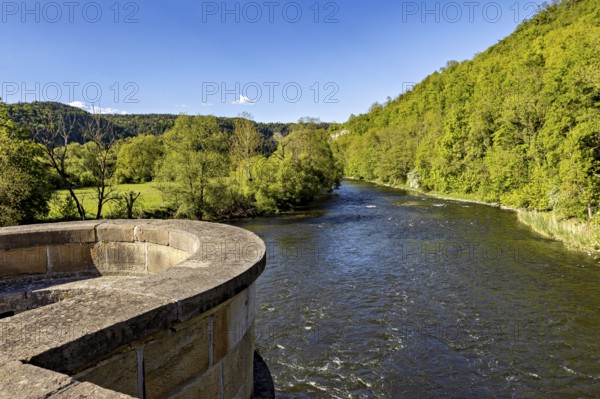 River next to a stone bridge, surrounded by forest under a blue sky, view from the historic Werra