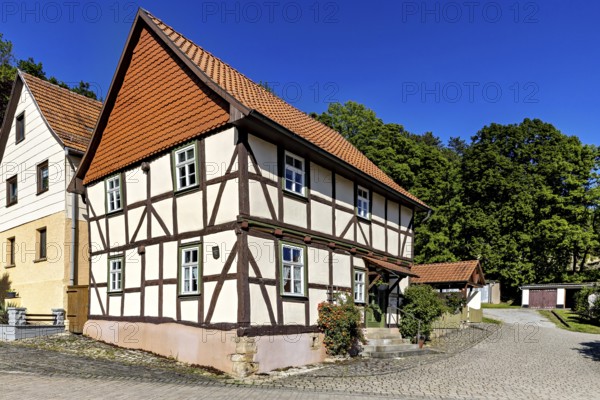 A picturesque half-timbered house with red roof tiles under a bright blue sky in the countryside,