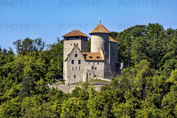 A medieval castle with two towers on a wooded hill under a blue sky, Normannstein Castle near