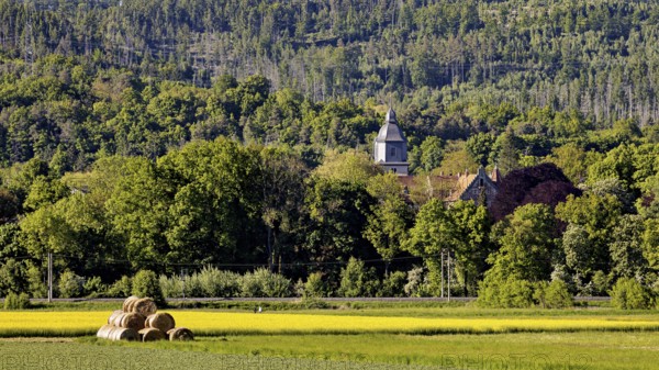 Landscape with church in the forest background and hay bales in the foreground, The church tower of