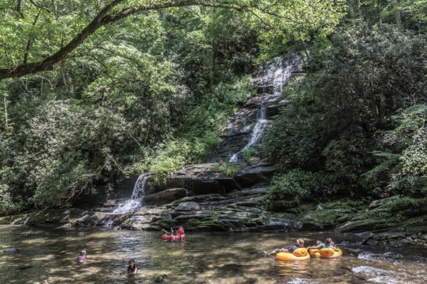 Visitors swimming and floating on inflatables at the base of Tom Branch Falls along Deep Creek in
