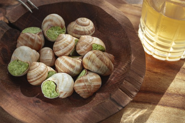 Snails cooked with herb oil on a wooden plate, served with white wine, natural light, no people