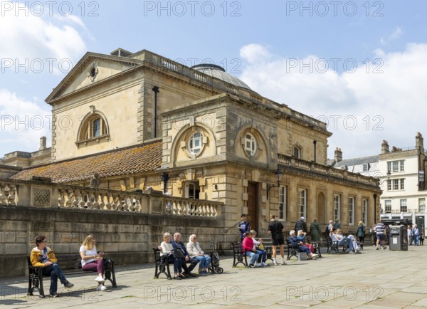 People relaxing next to Roman Baths building, Abbey church yard, city of Bath, north east Somerset,